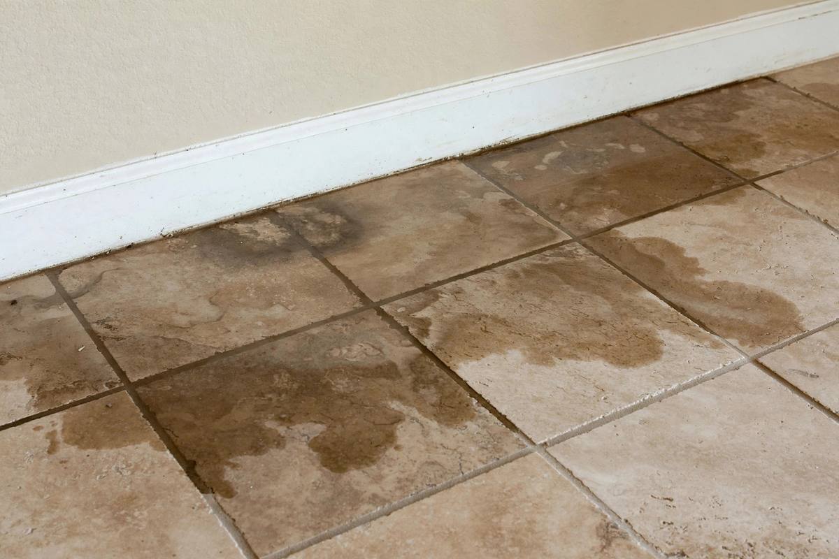 Water stain spreading across tile flooring near a baseboard in an Arizona home